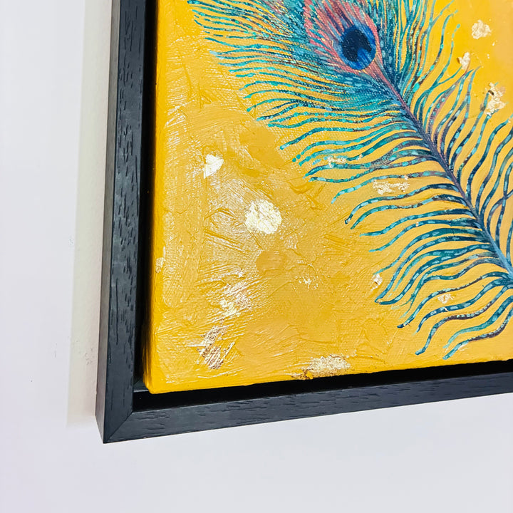 Framed artwork of a peacock feather on a yellow background