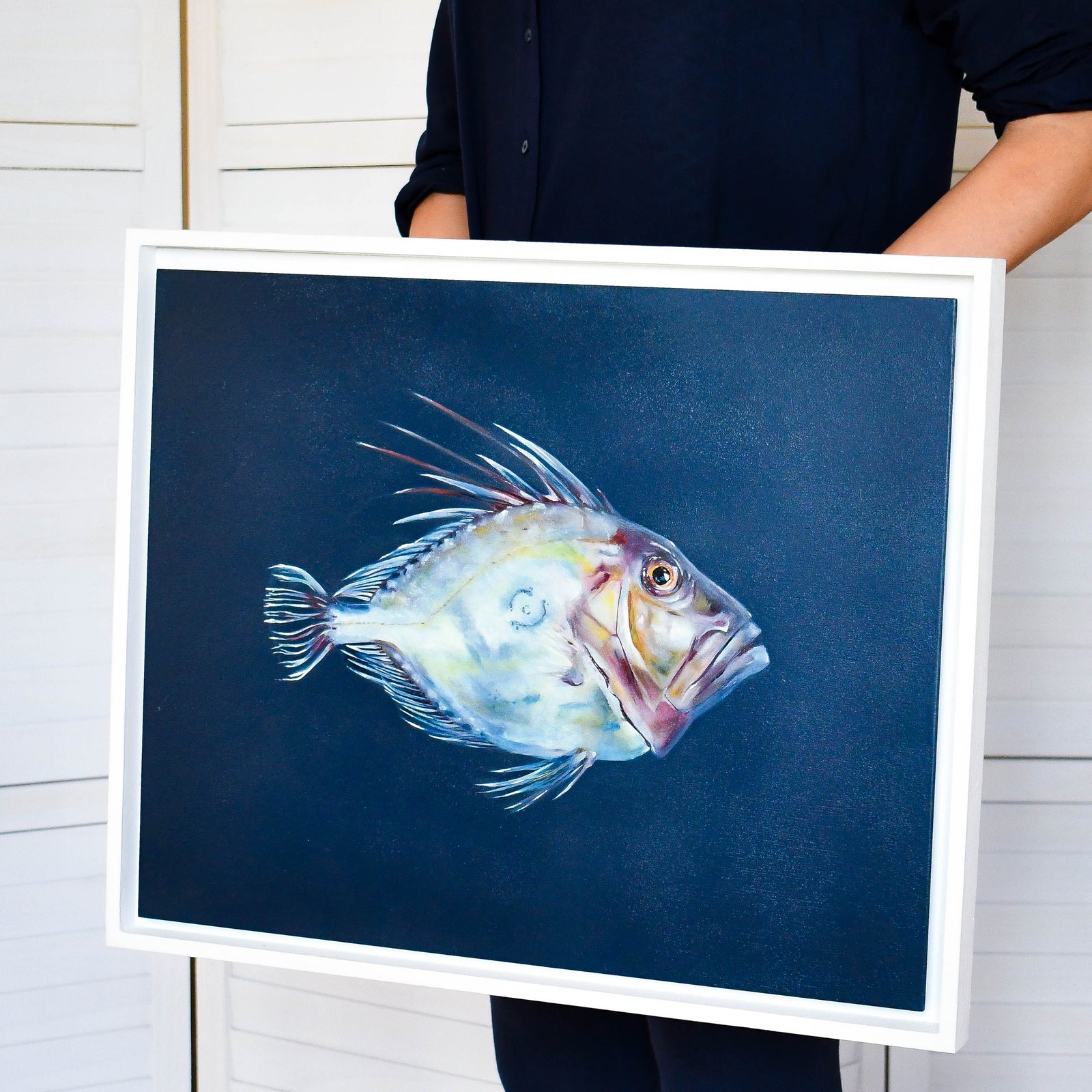 Person holding a framed painting of a fish on a blue background