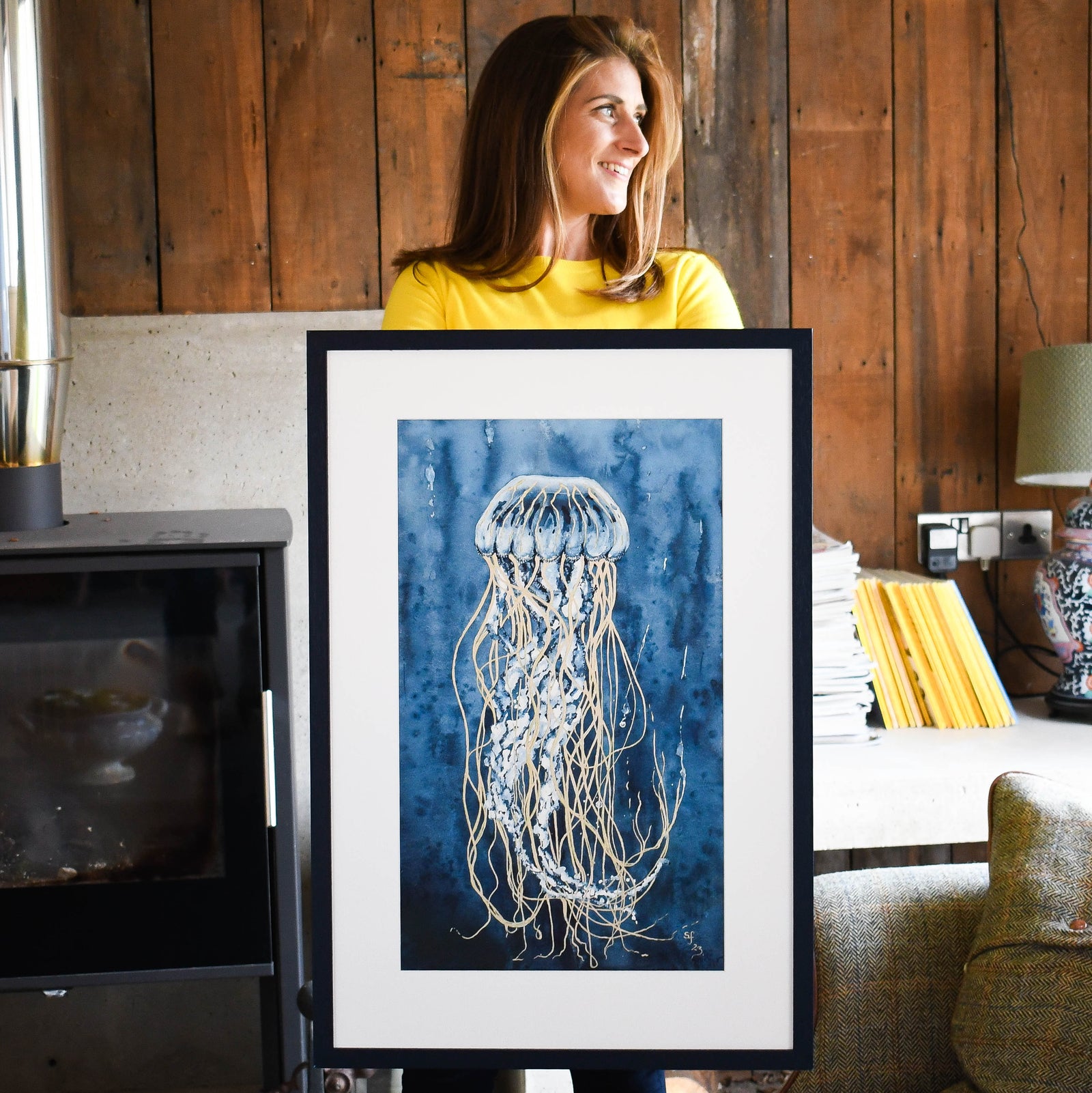 Woman holding a framed artwork of a jellyfish in a room with wooden walls.