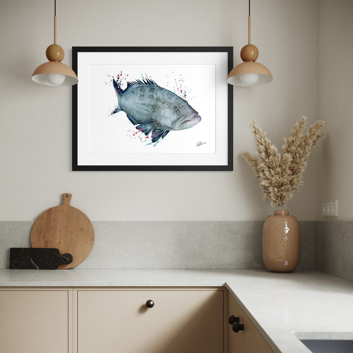 Framed artwork of a fish on a kitchen wall with a vase and cutting board.