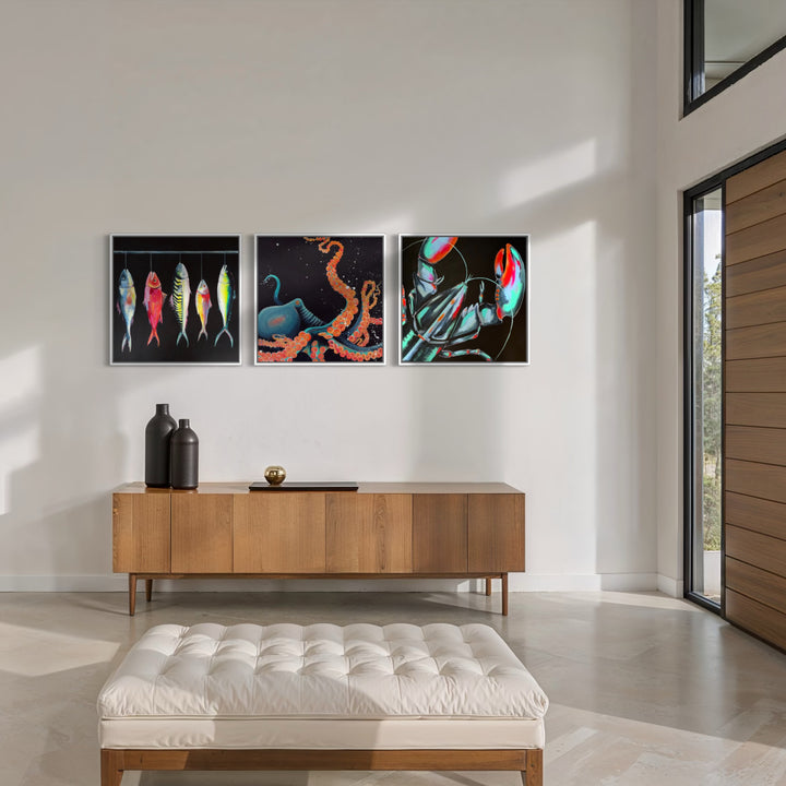 Three framed abstract art prints are displayed on a white wall above a mid-century modern wooden credenza in a bright, contemporary living room. The prints feature colorful abstract designs: three fish on a black background, an orange tentacle on a dark background, and a red and blue astronaut helmet on a black background.