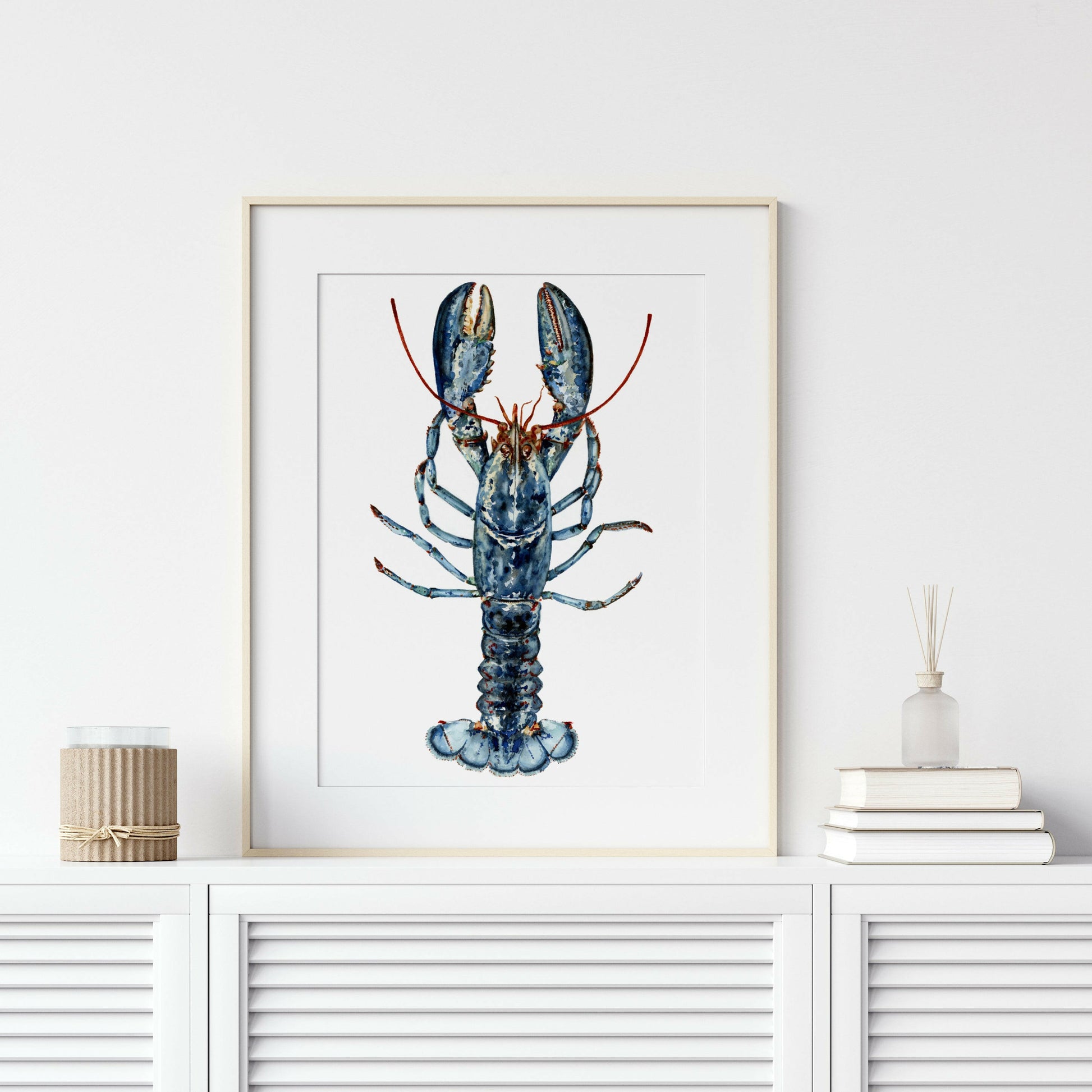 Blue lobster watercolour on a white background, in a light wood frame, on a white shelf and  white  wall
